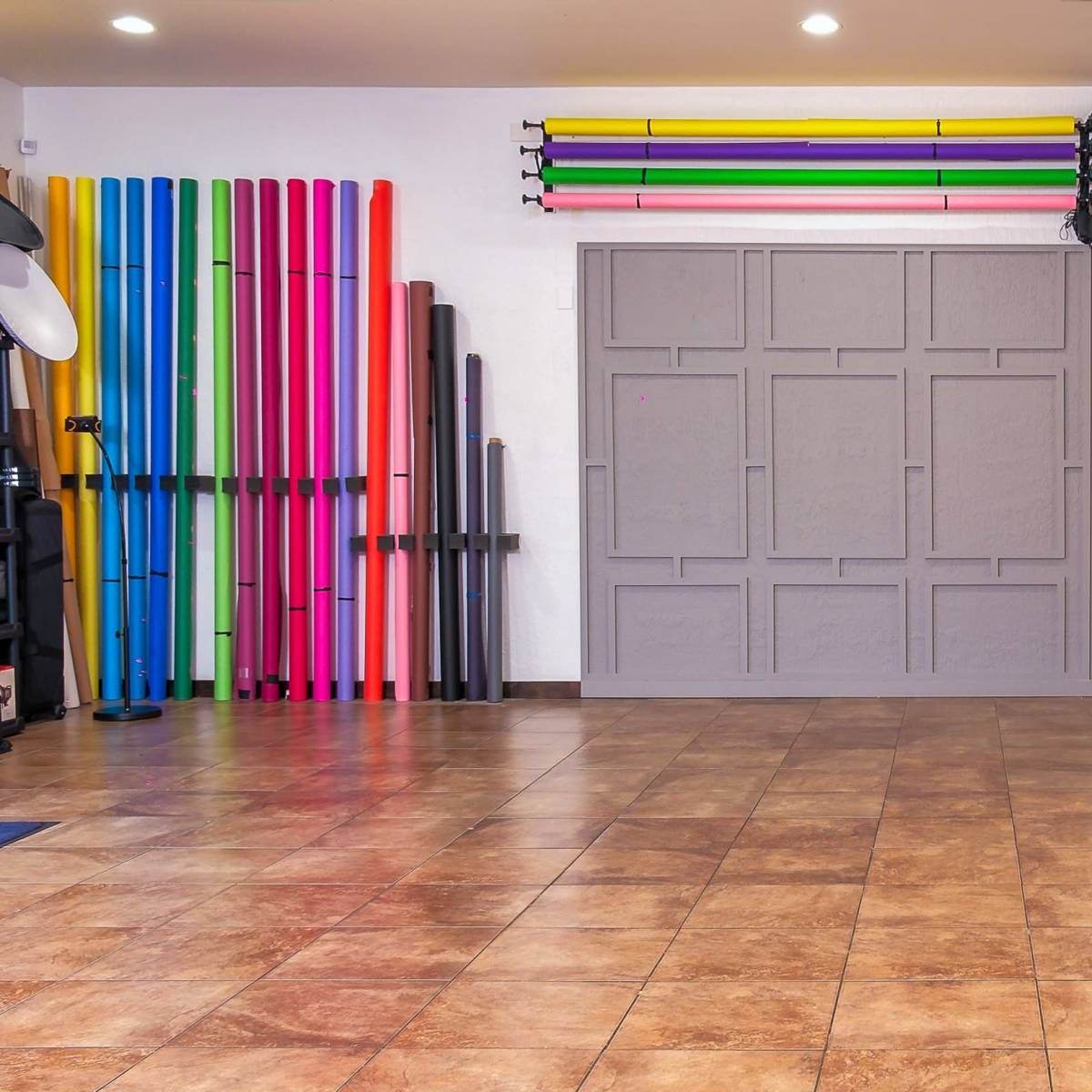 A spacious studio interior with tiled flooring, featuring colorful backdrop rolls on the wall and two different textured panels.