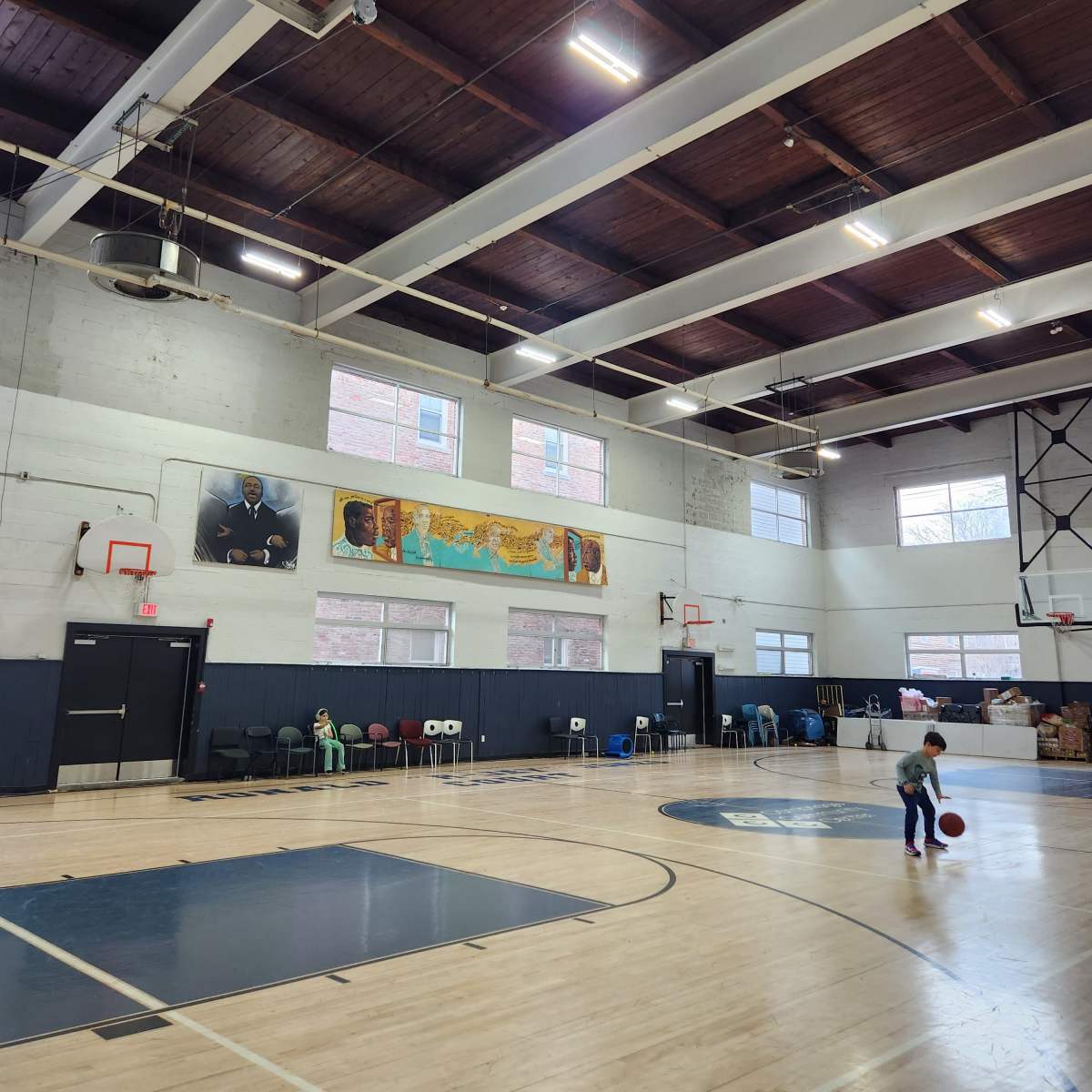 A gymnasium with a basketball court, high ceilings, and a child playing with a basketball.