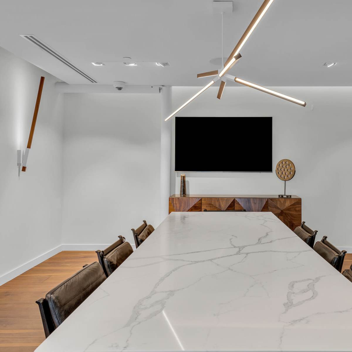 A modern conference room features a long marble table, a wall-mounted television, and minimalist wooden accents.