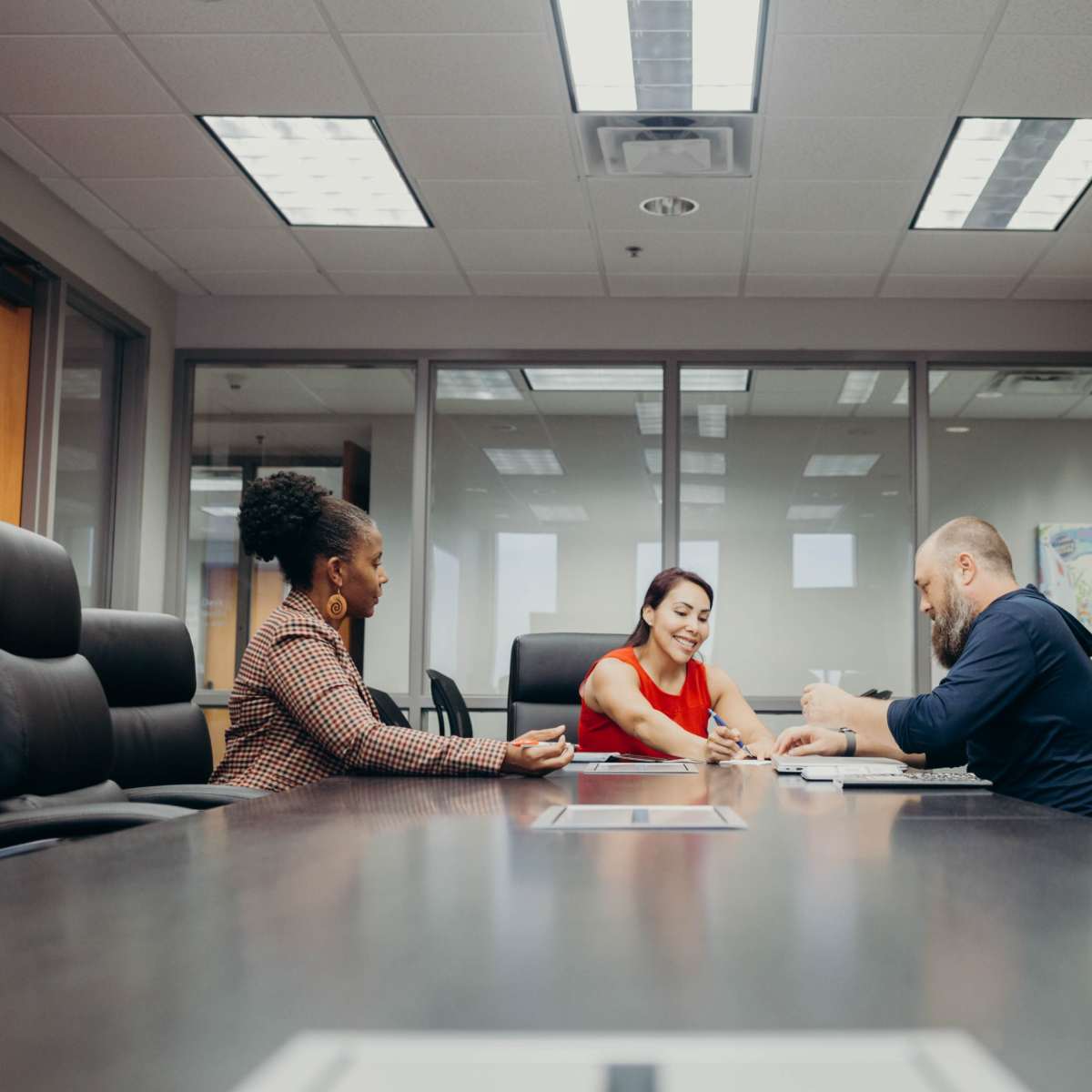 Three colleagues hold a meeting around a conference table in a well-lit office.