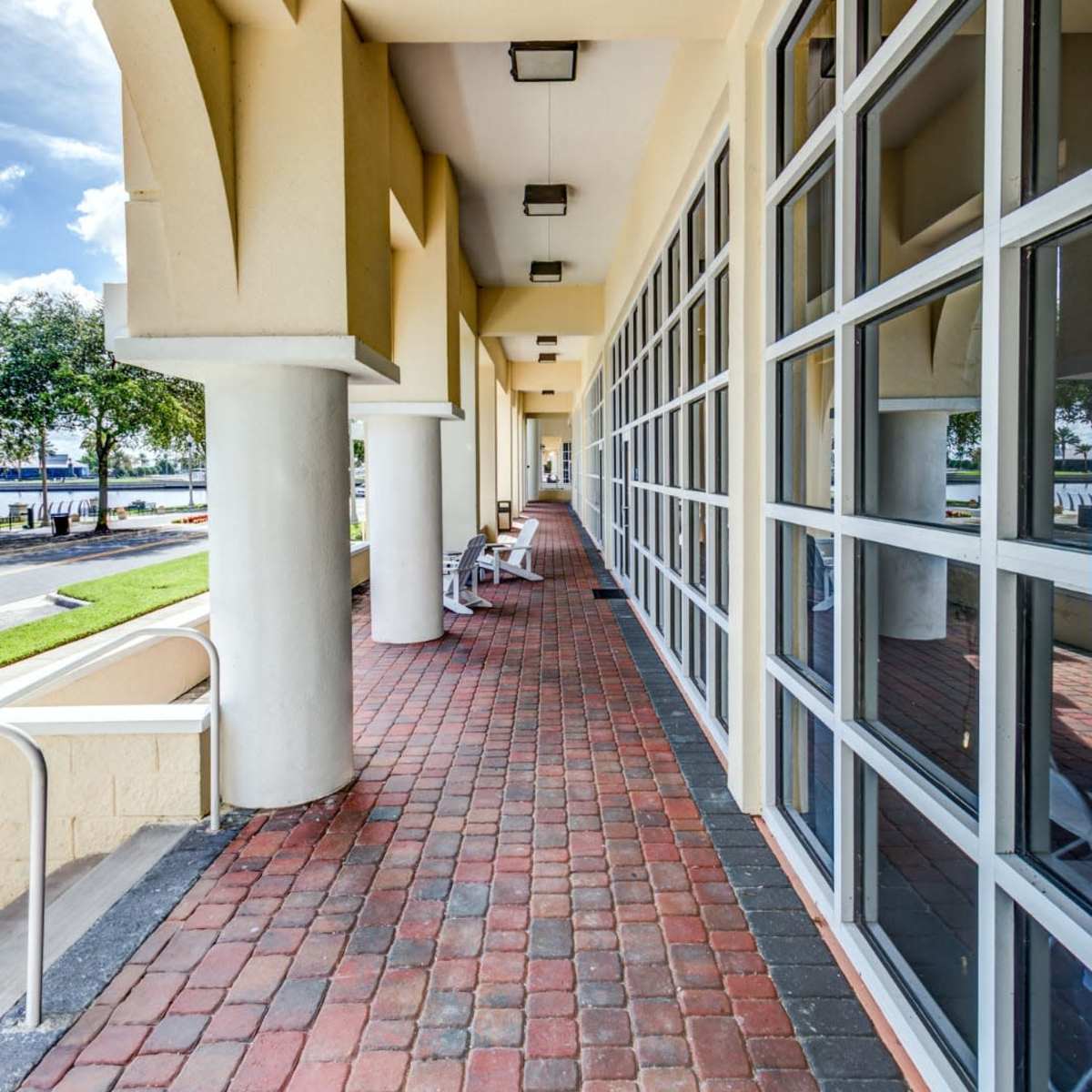 A brick-lined walkway bordered by large windows and columns, leading to an outdoor view.