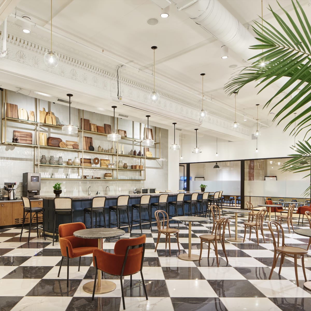 A spacious café interior with a checkerboard floor, shelves displaying wooden items, and a seating area featuring various chairs and tables.