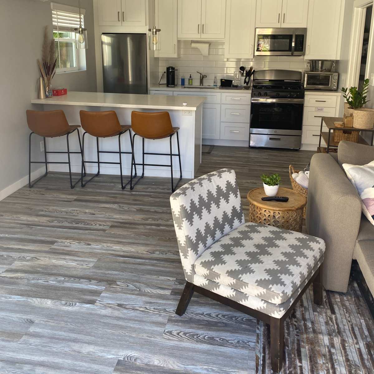 A modern kitchen features white cabinets, stainless steel appliances, and a breakfast bar with three brown stools.