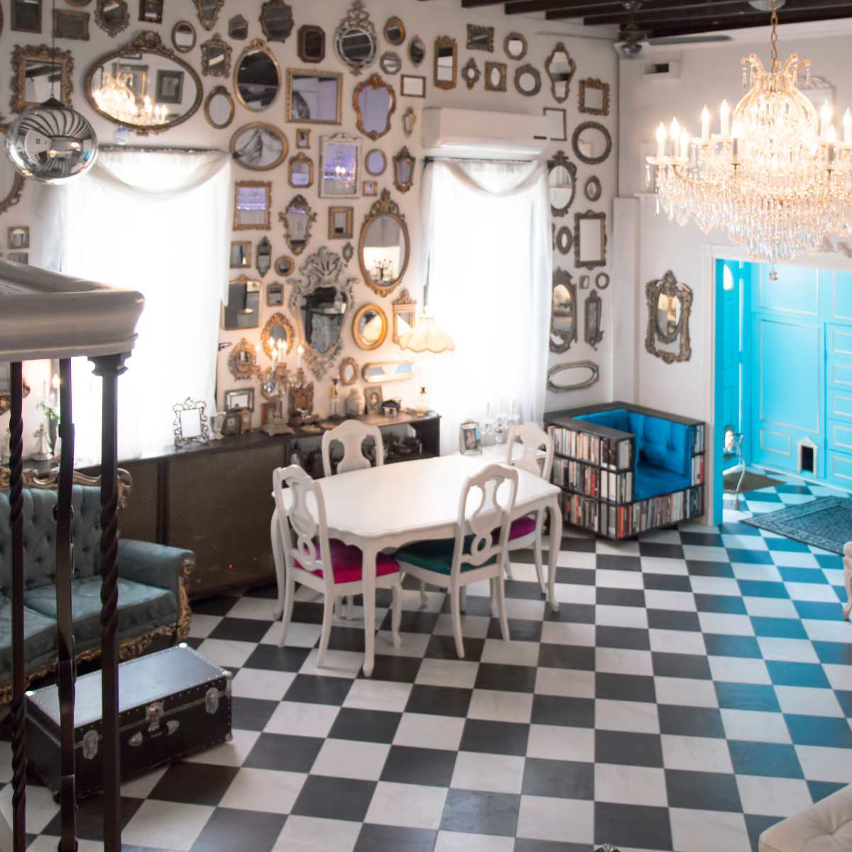 A spacious room with black and white checkered flooring, adorned with numerous decorative mirrors on the walls, a chandelier overhead, and a white dining table surrounded by elegant chairs.