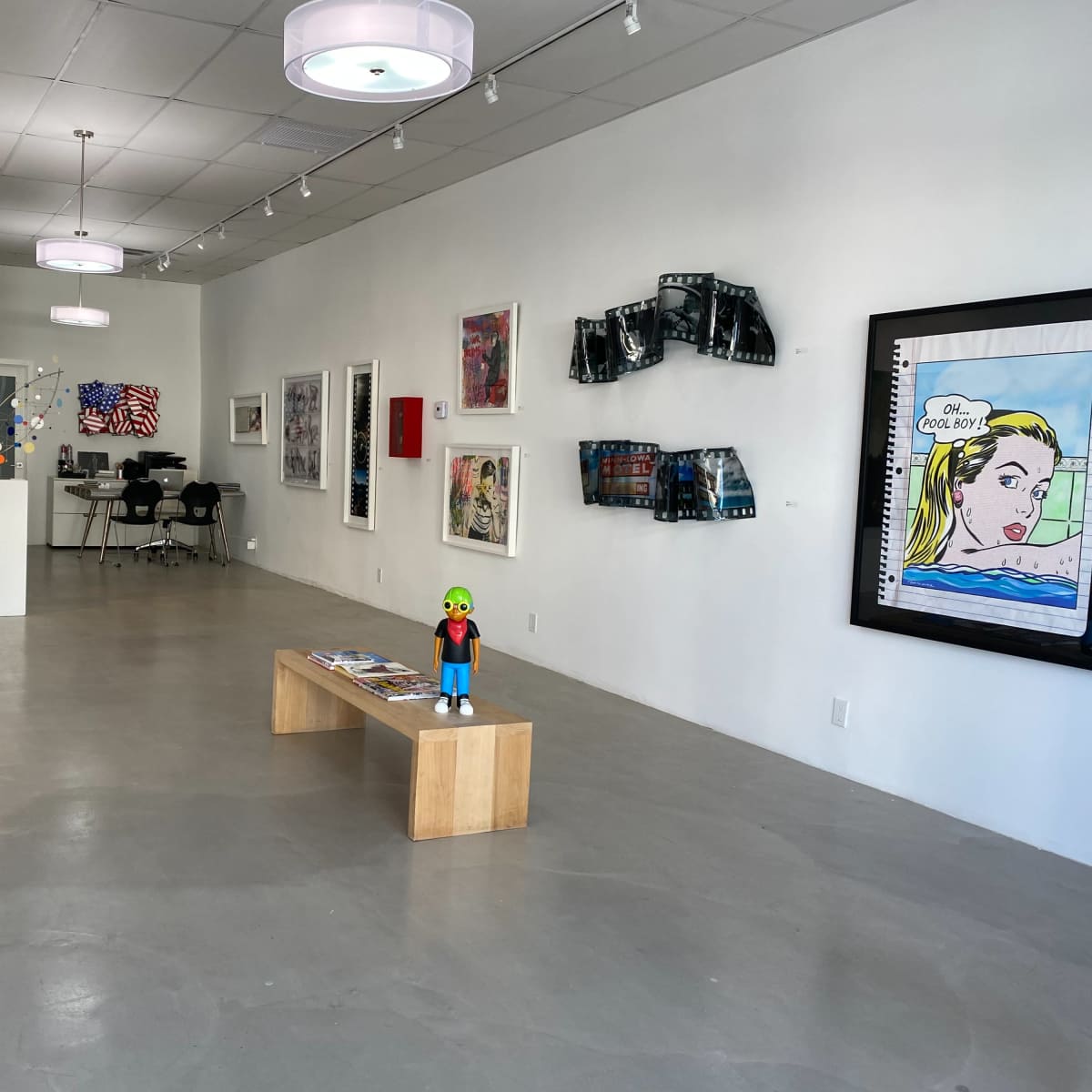 An art gallery featuring various artworks displayed on the walls, a wooden bench in the center, and modern furniture in the background.