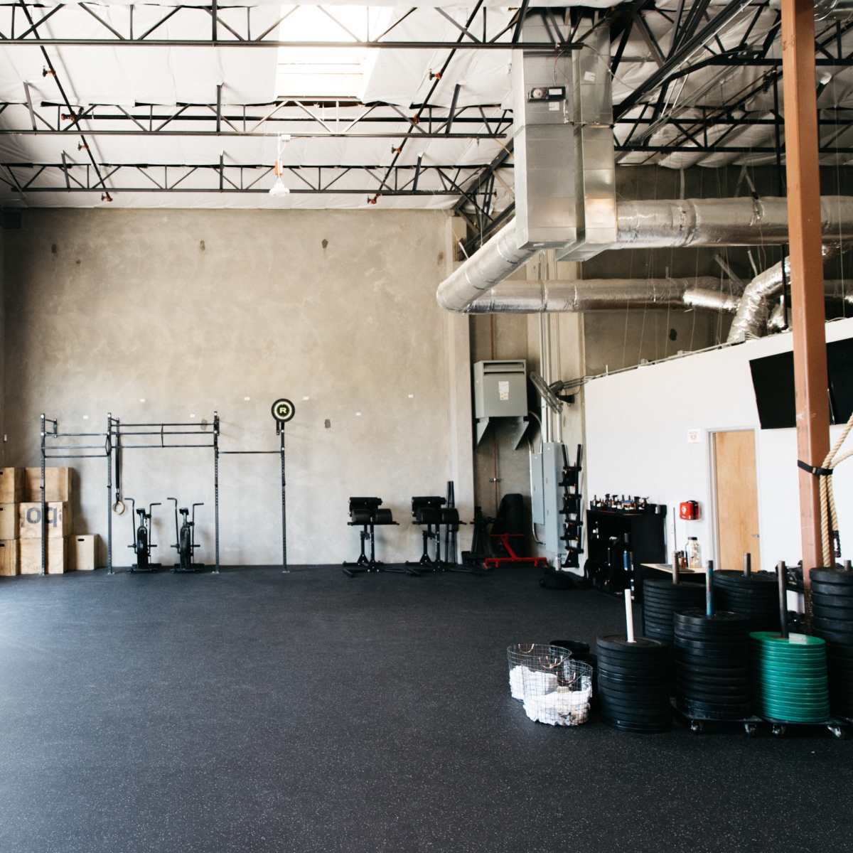A spacious fitness gym with gray walls, rubber flooring, and various gym equipment arranged along one side.