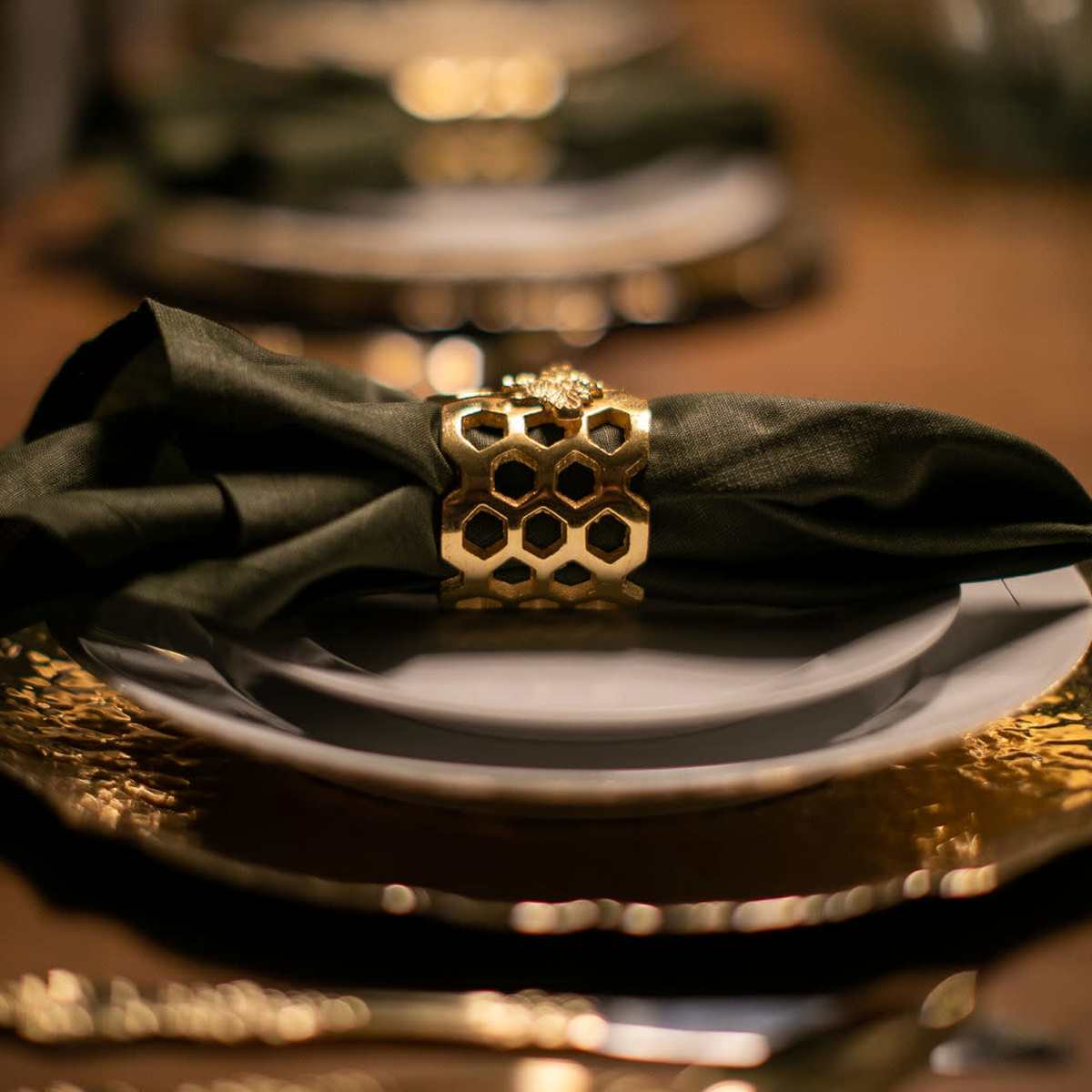 A beautifully set dining table features elegant plates, gold accents, and dark green napkins secured with decorative holders.