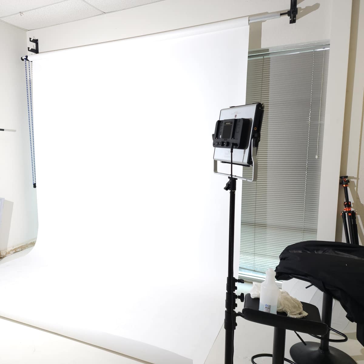 A photography studio with a white backdrop, lighting equipment, and a mirror positioned nearby.