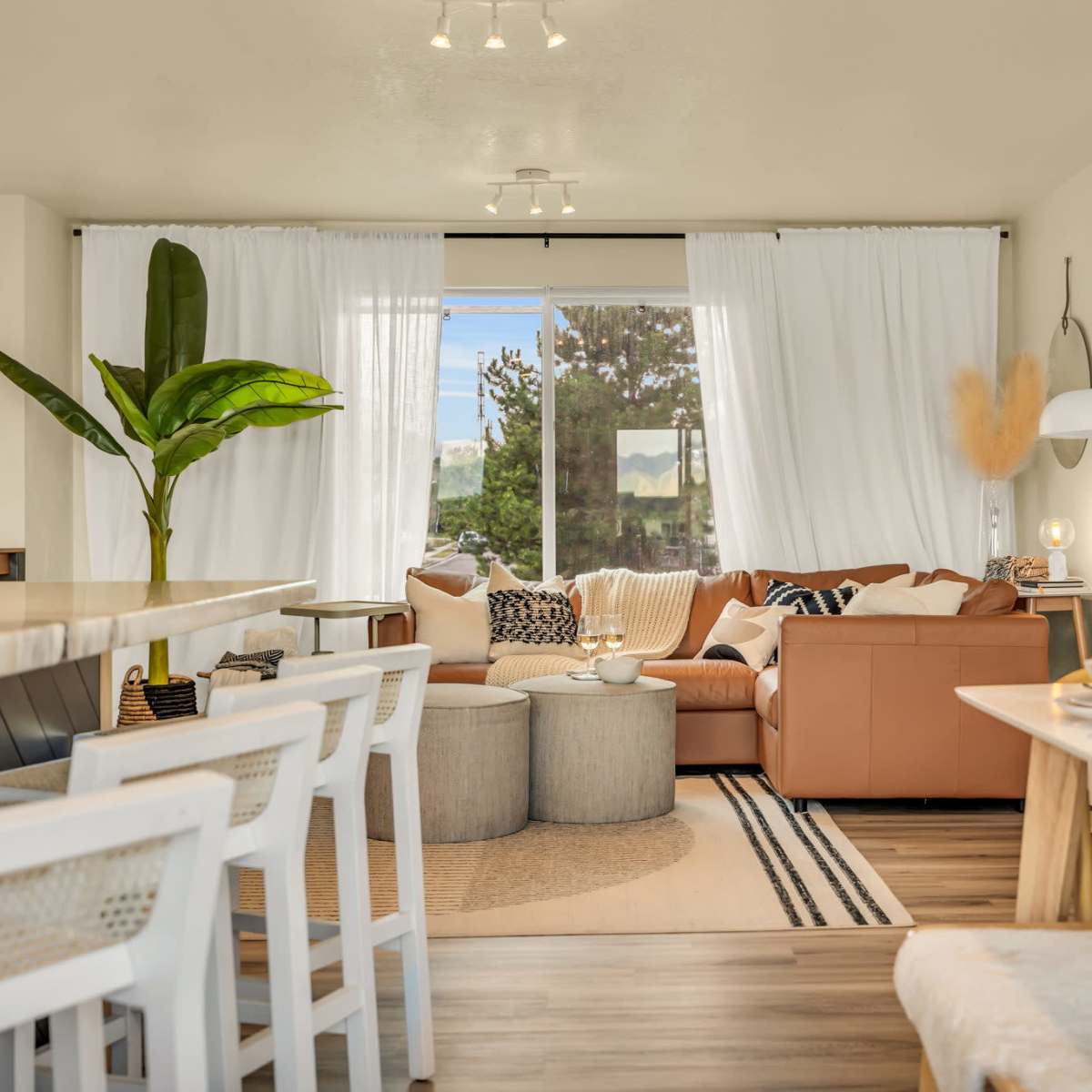 A modern living space with a sectional sofa, a dining area, and large windows draped with sheer curtains.