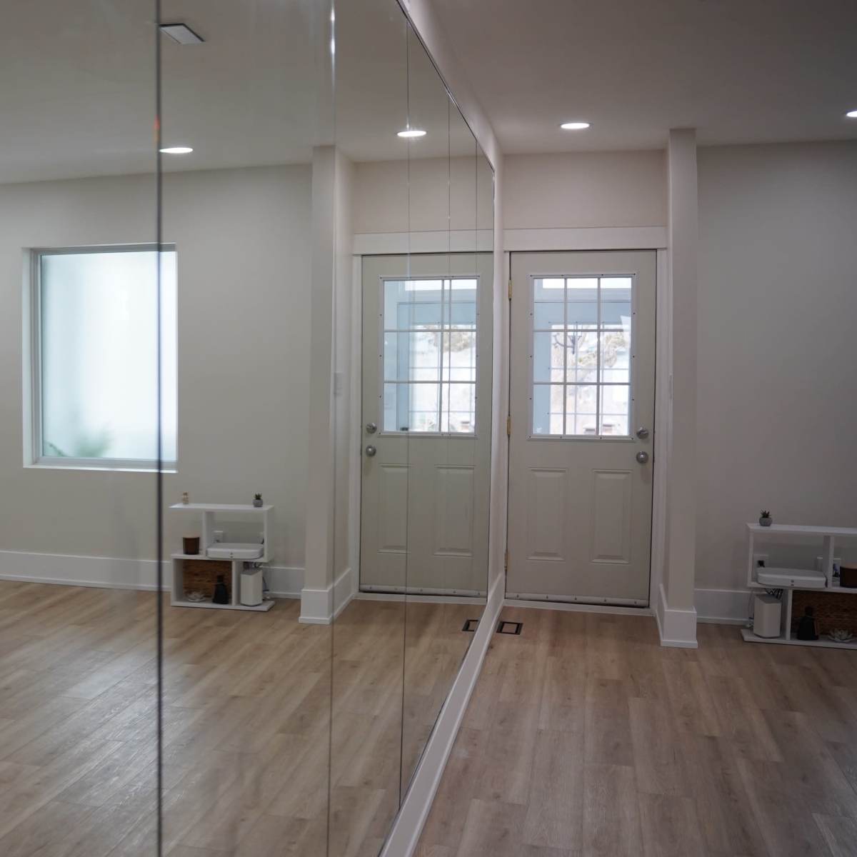 A spacious, well-lit room with a wall of mirrors, a television mounted on one wall, and a door leading outside.