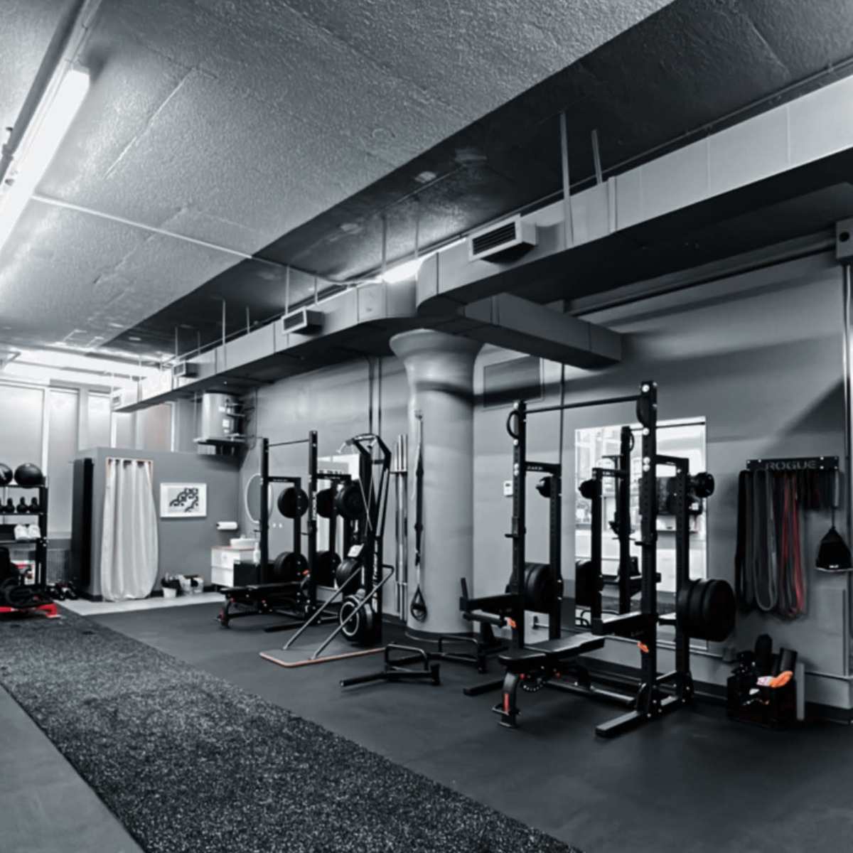 An empty gym interior with various weightlifting equipment arranged along the walls and a rubber flooring surface.