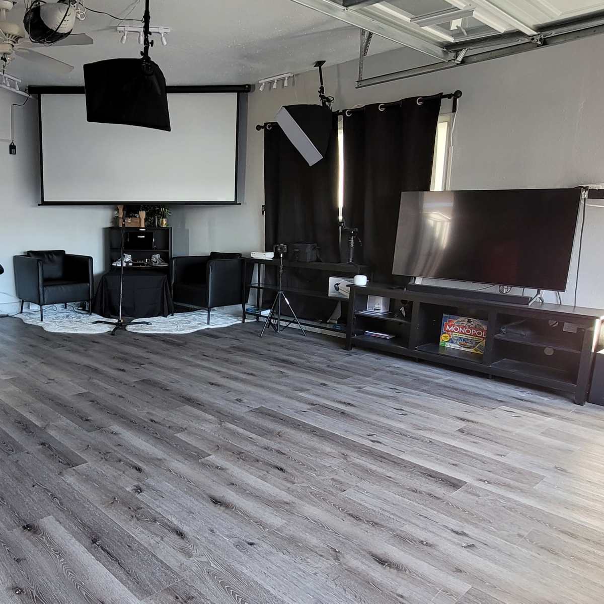 The room features a large, empty space with a smooth floor, equipped with a projection screen, a TV, several black chairs, and softbox lighting setups.