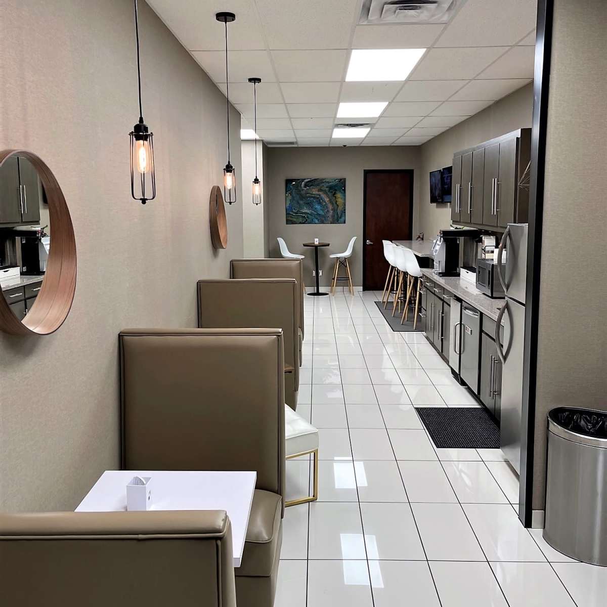 A modern, well-lit hallway with booths on either side, white tile flooring, and kitchen cabinets along one wall.