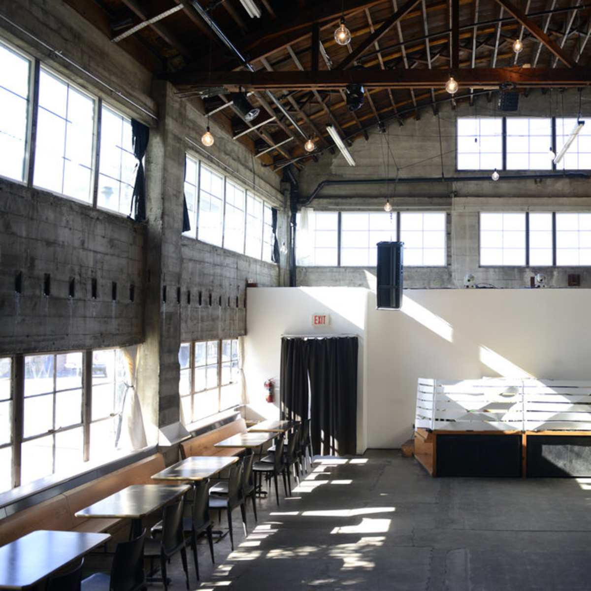 The interior of a spacious venue with large windows, exposed wooden beams, and a stage area at one end.
