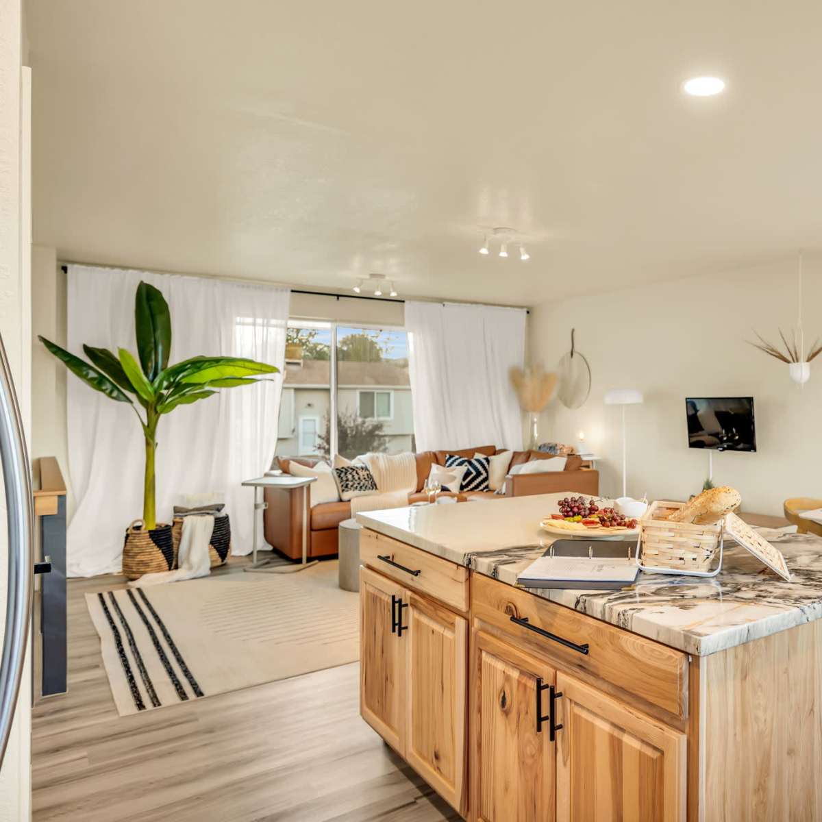 A modern living space features a kitchen island, dining area, and a seating area with a large window.