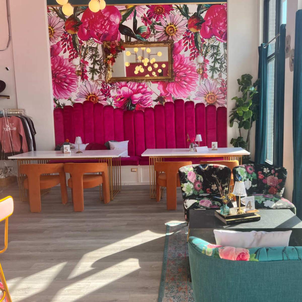 A brightly decorated café interior featuring floral wallpaper, vibrant seating, and large windows allowing natural light to fill the space.