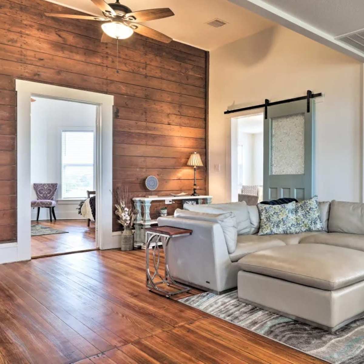 A modern living room featuring a light-colored leather sectional sofa, a wooden accent wall, and a sliding barn door.