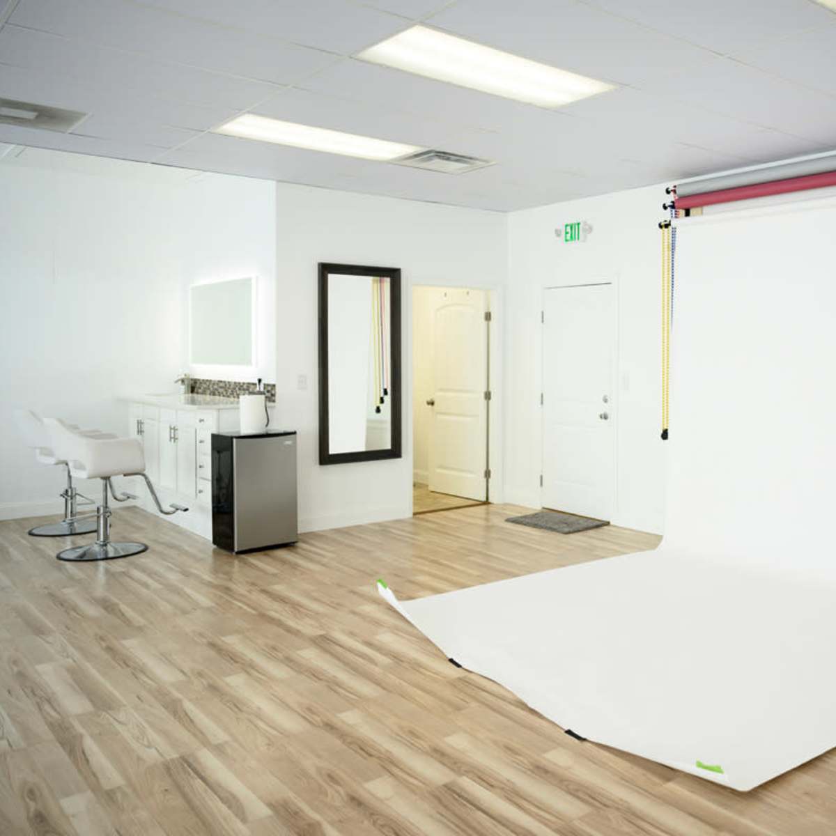 A spacious studio with a white backdrop set up for photography, featuring a mirror, a small counter, and modern seating.