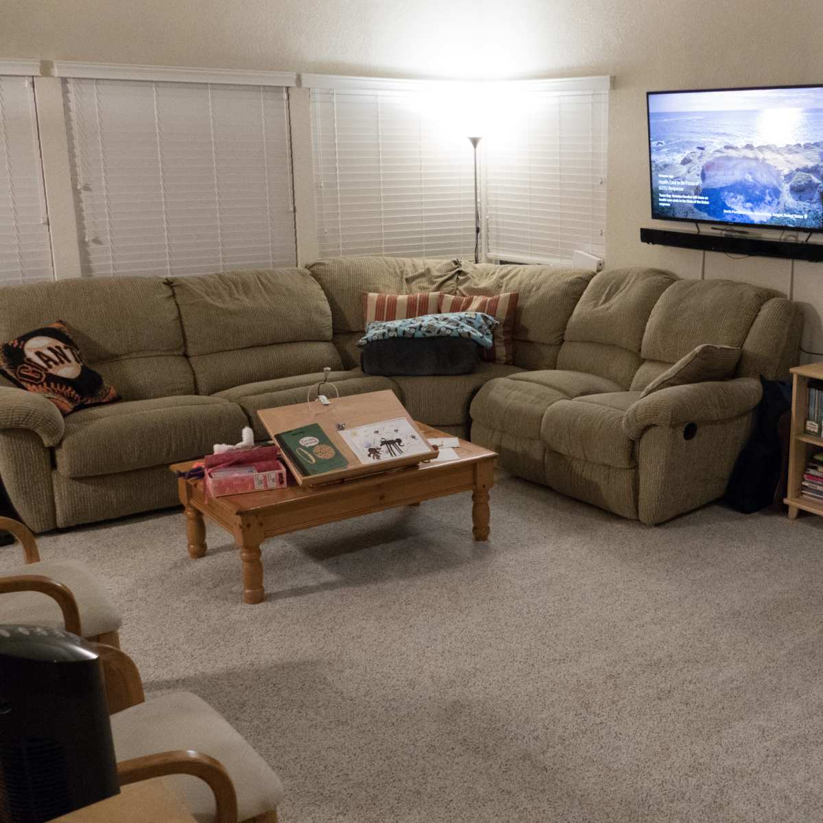 The living room features a sectional couch facing a wall-mounted television, with a wooden coffee table and a bookshelf full of books in the corner.
