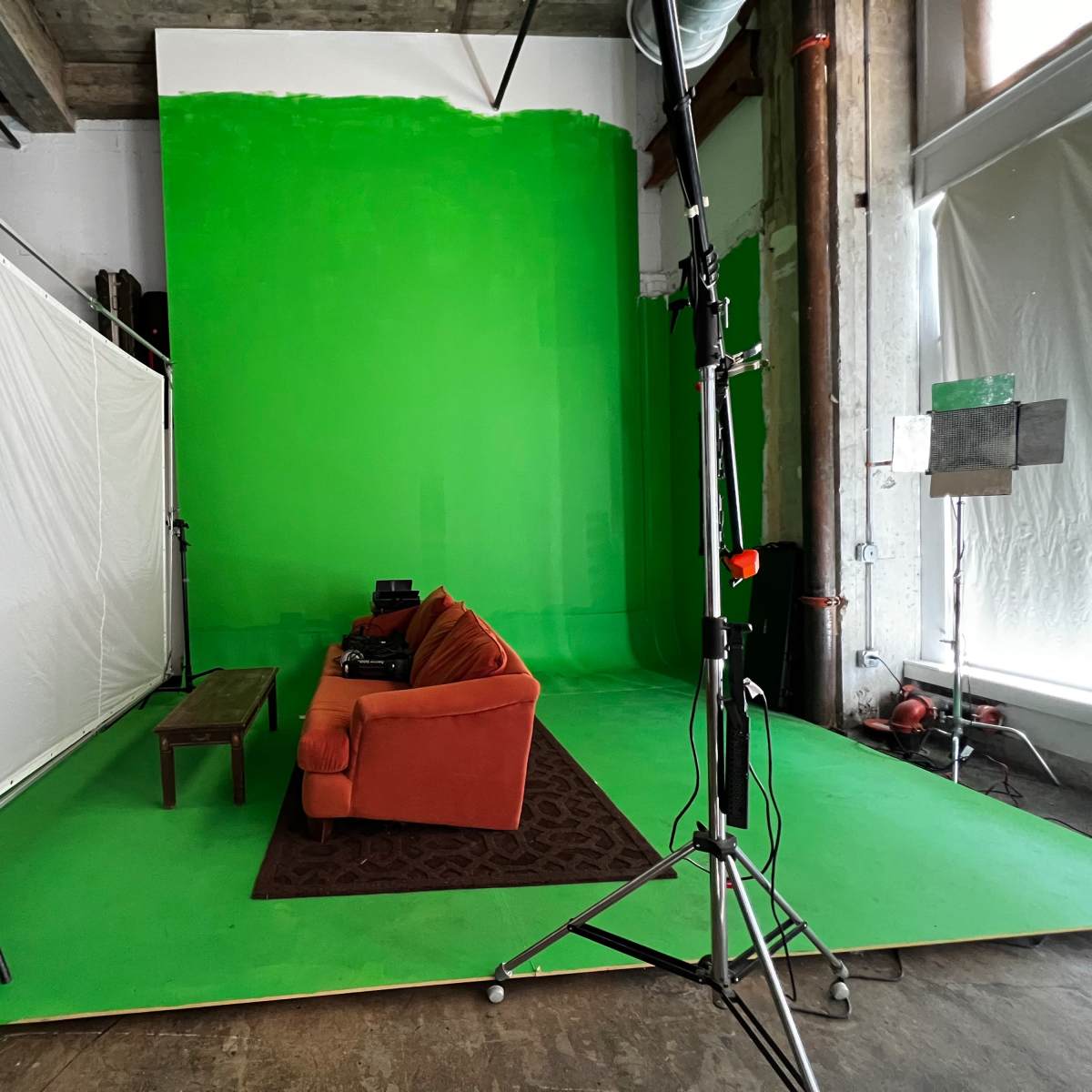 A green screen studio setup featuring an orange couch, a coffee table, and a patterned rug on a green floor.
