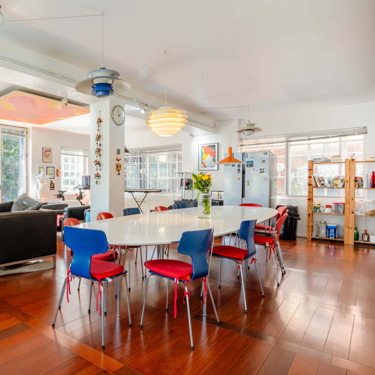 A spacious, modern open-concept living area features a dining table surrounded by colorful chairs, a large sofa, and multiple windows allowing natural light to fill the space.