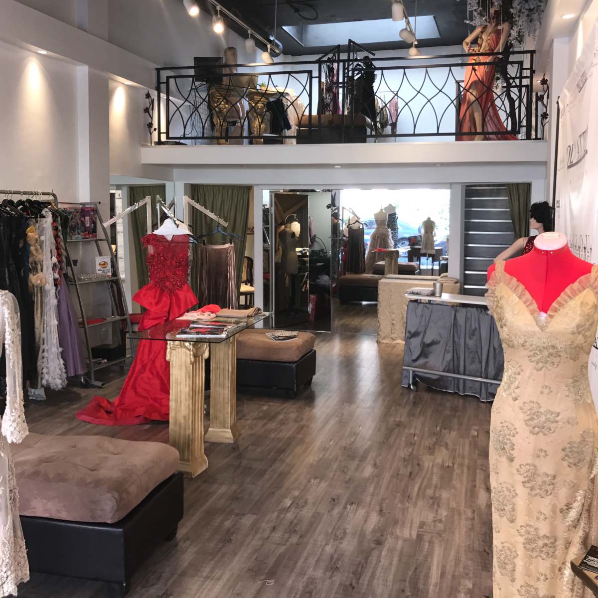 An interior of a dress boutique featuring elegant garments displayed on mannequins and clothing racks, with a staircase leading to a second-level section.