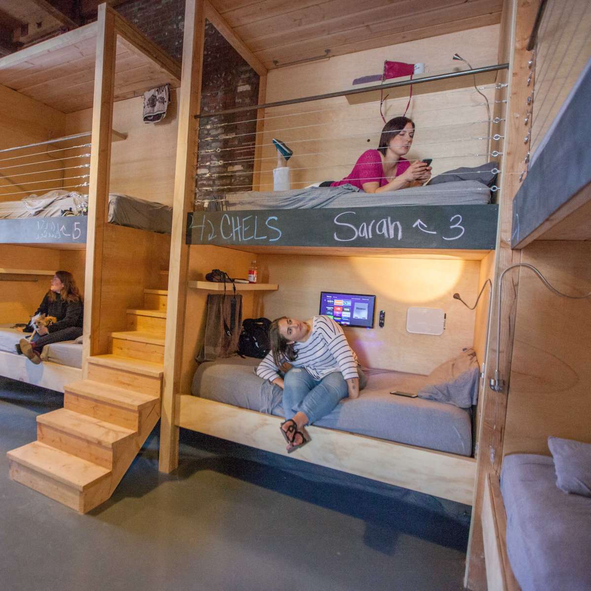 A shared dormitory with bunk beds, where two occupants are resting, one person is on a phone, and another is standing nearby.