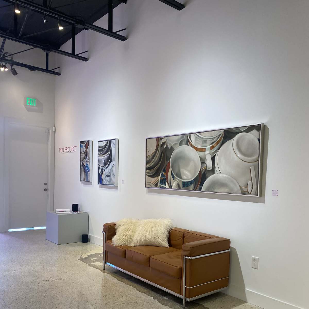 A minimalist art gallery featuring a brown leather couch, a white decorative pillow, and framed artworks on the walls.