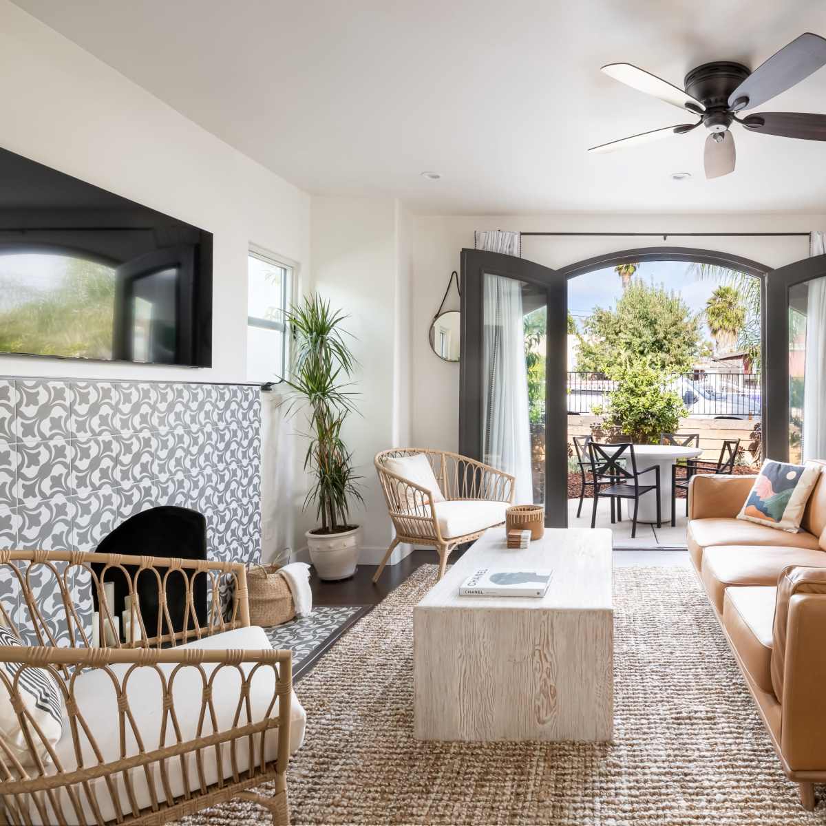 The living room features a leather sofa, wicker chairs, a wooden coffee table, and large arched doors leading to an outdoor patio.