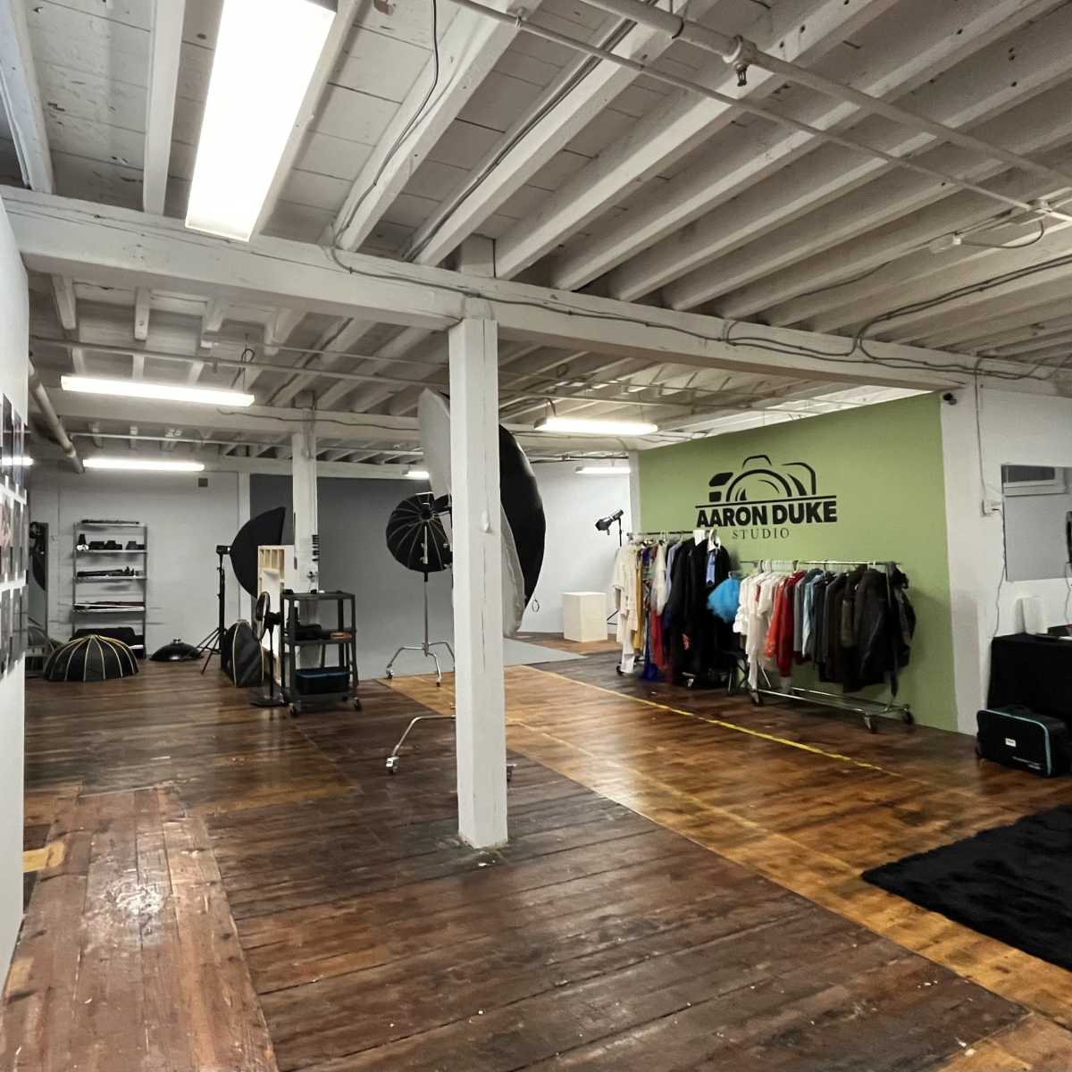 A spacious photography studio with a wall displaying framed portraits, clothing racks, and various photographic equipment.