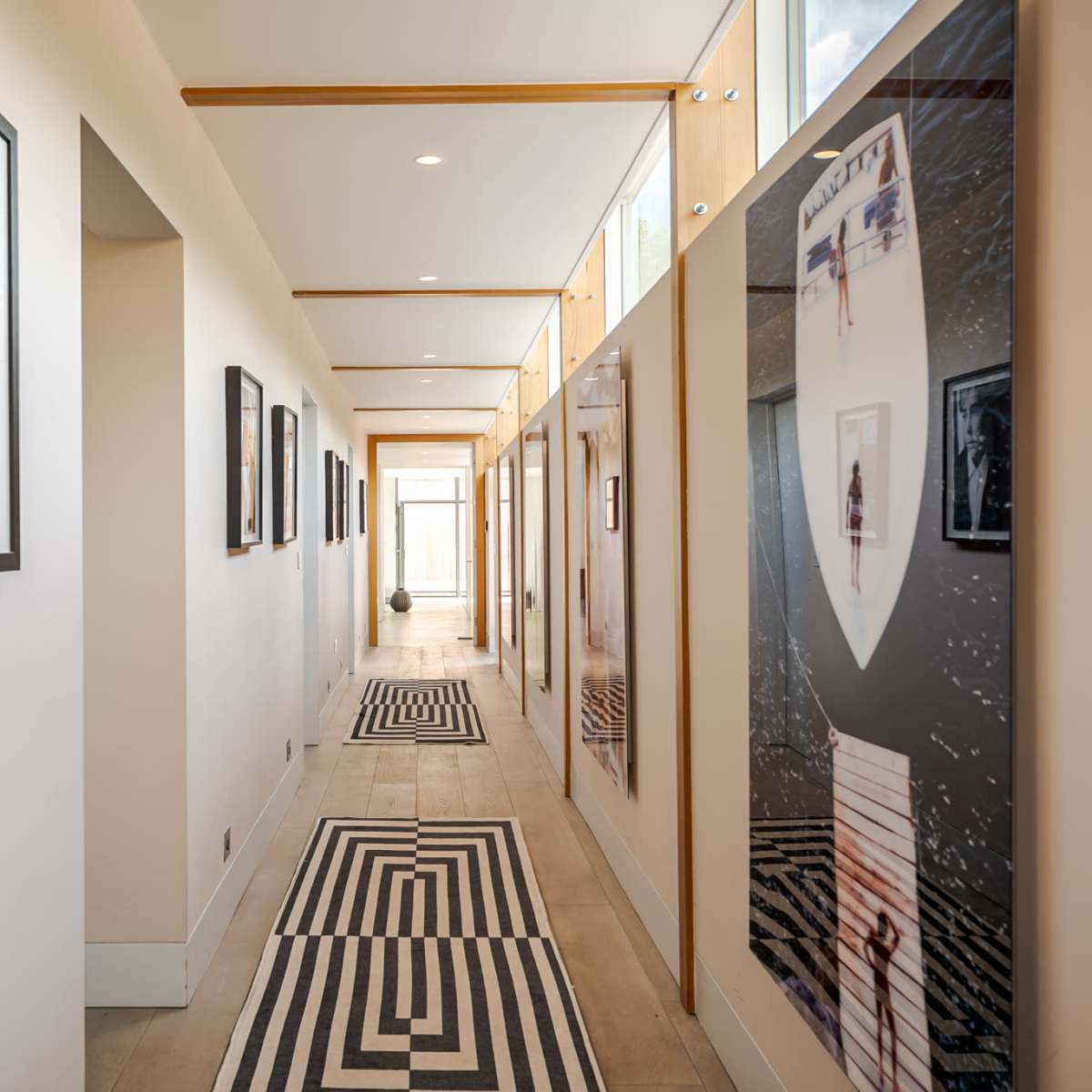 A modern hallway lined with framed photographs on both sides, featuring a striped black-and-white rug on the floor.