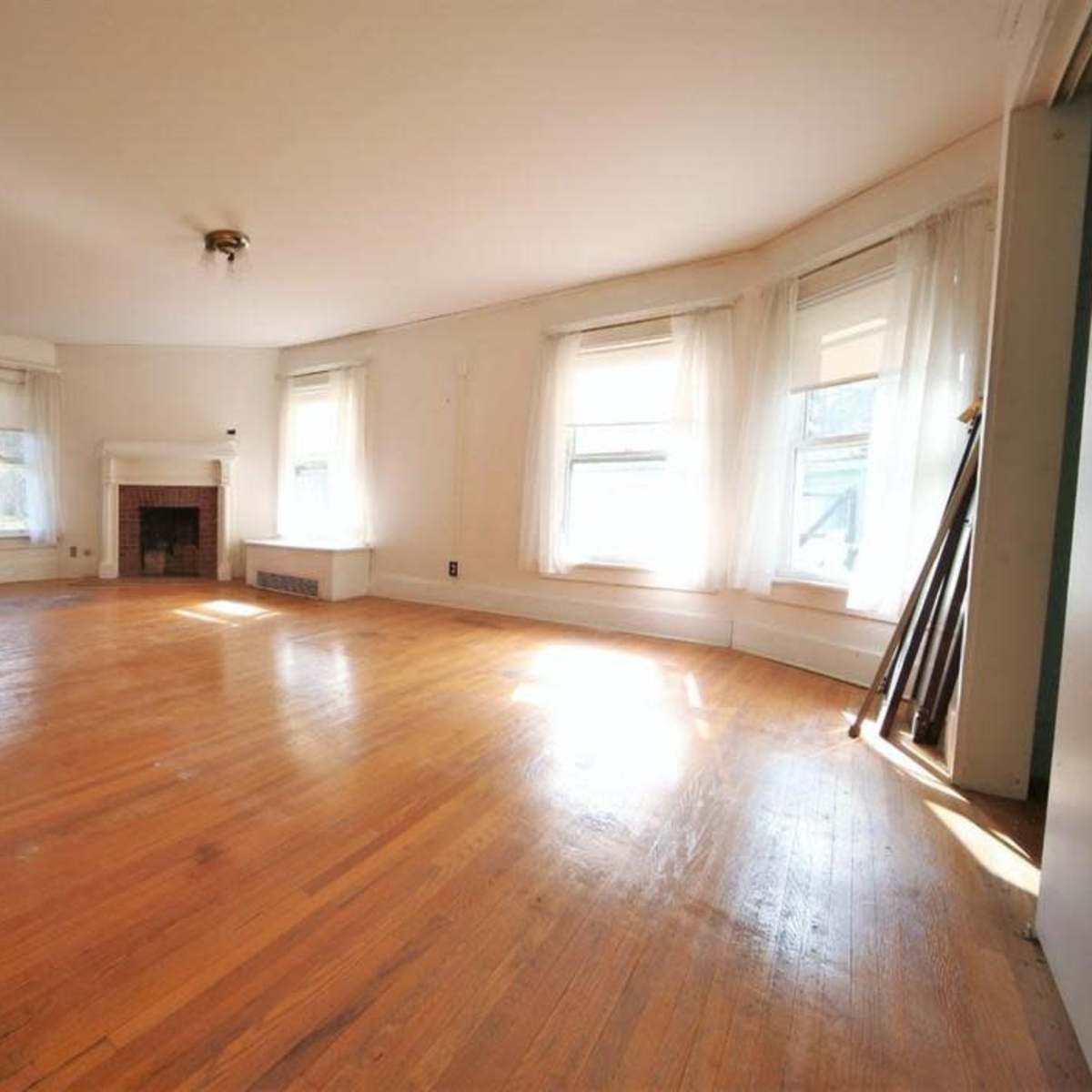 A bright, empty living room with hardwood floors, large windows, and a fireplace.