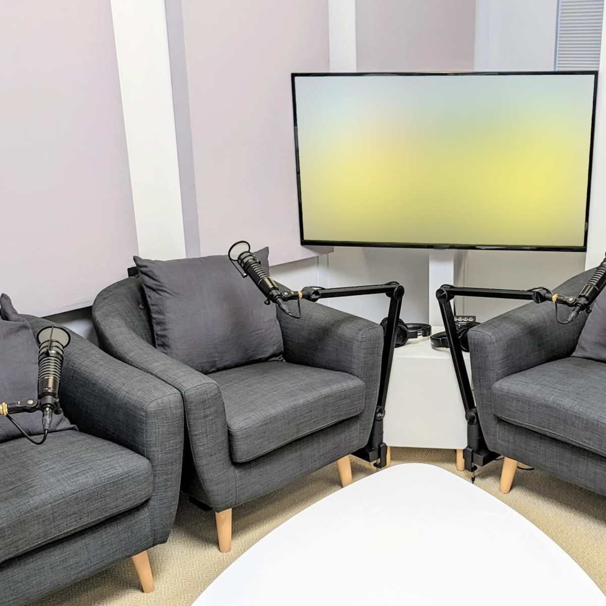 Four dark gray chairs arranged around a white coffee table, with a television mounted on the wall behind them.