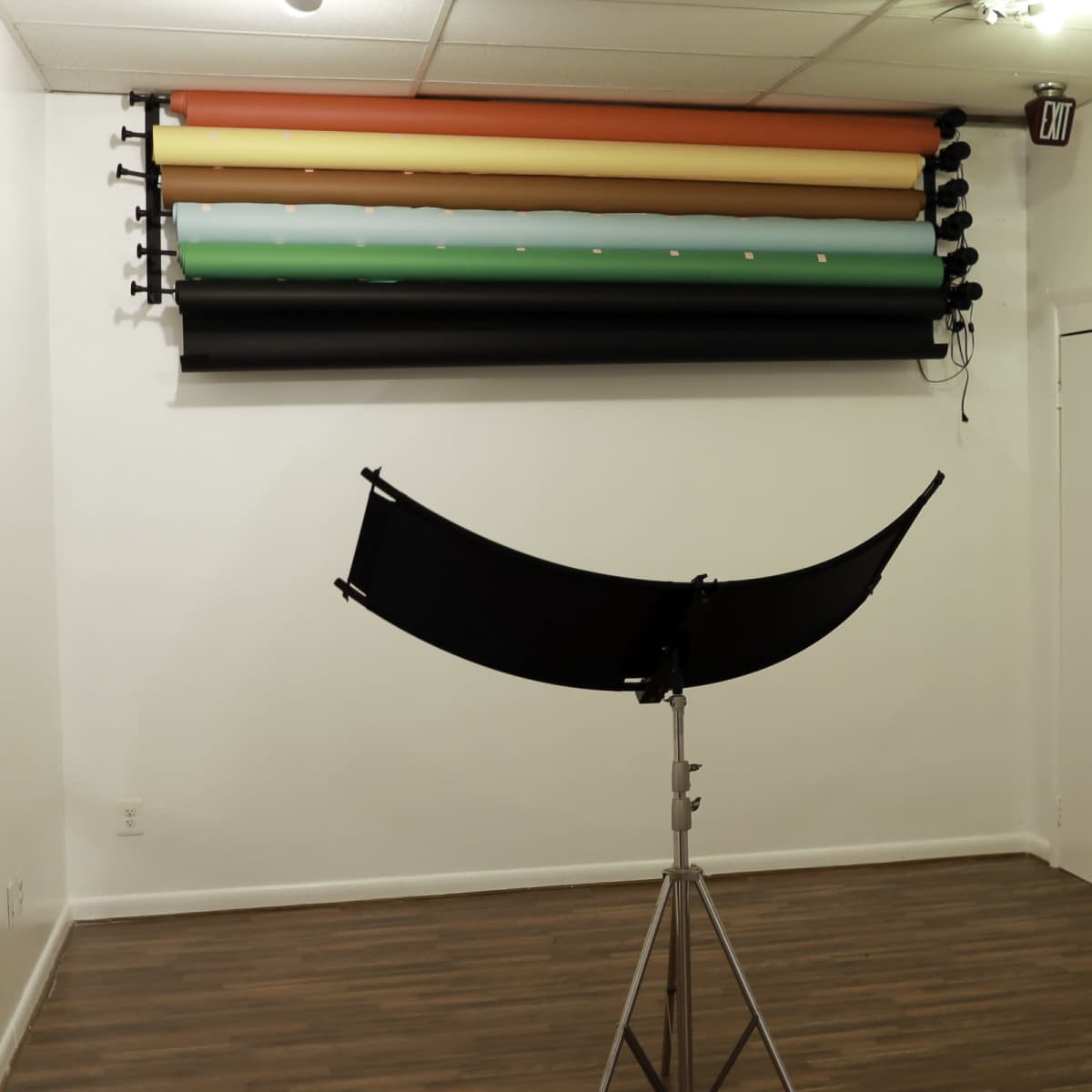 A photography studio with backdrop rolls hanging on the wall and a large umbrella softbox on a stand.