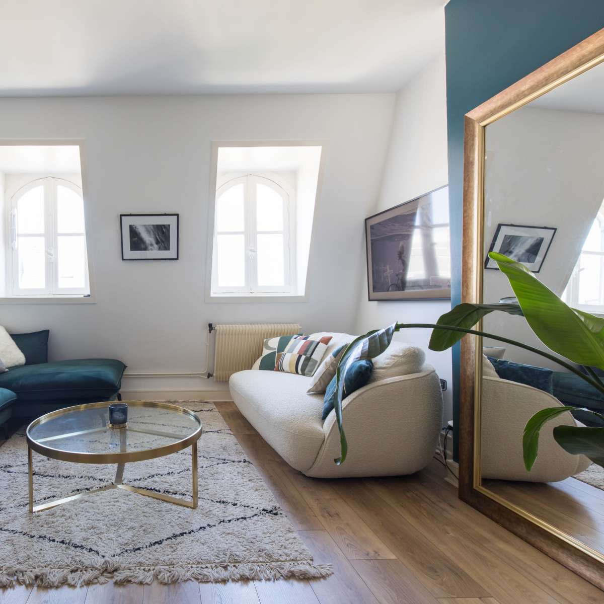 A modern living room with a green sofa, a light-colored couch, a glass coffee table on a textured rug, and several framed pictures on the walls.