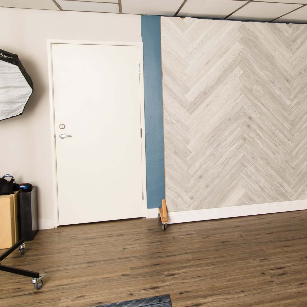 A room with a herringbone-patterned wall, a closed door, and wooden flooring.