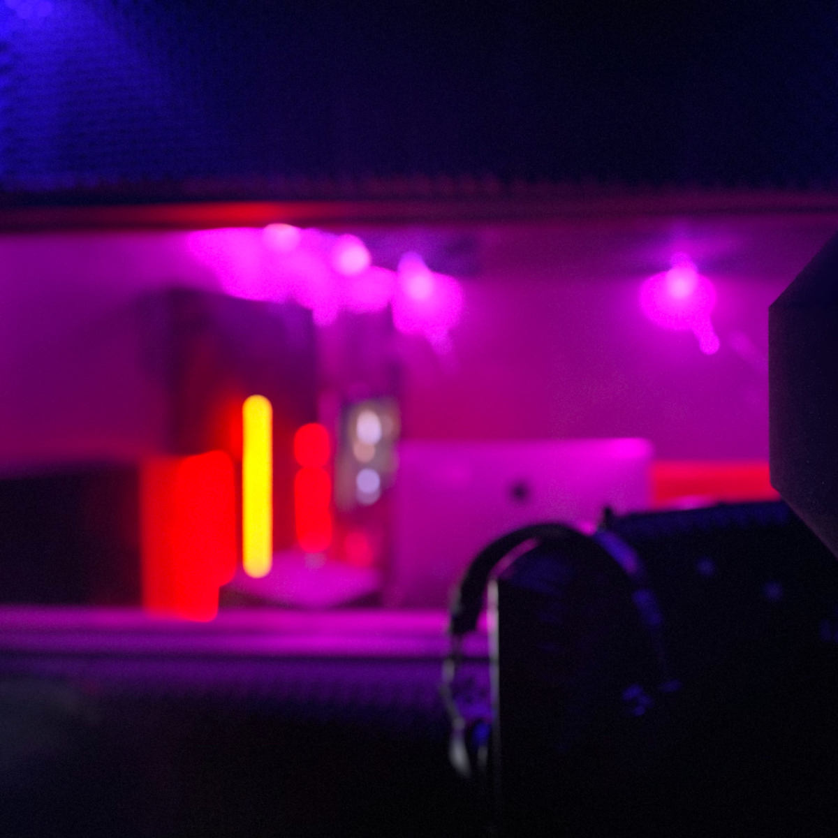 A dimly lit recording studio with purple and red lights illuminating equipment and a microphone in the foreground.
