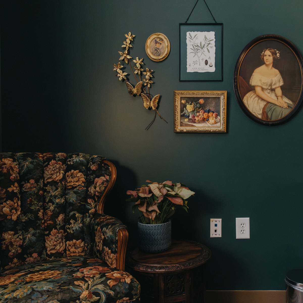 The scene features a floral-patterned couch beside a wall adorned with various framed artworks and a wooden vanity with a mirror.