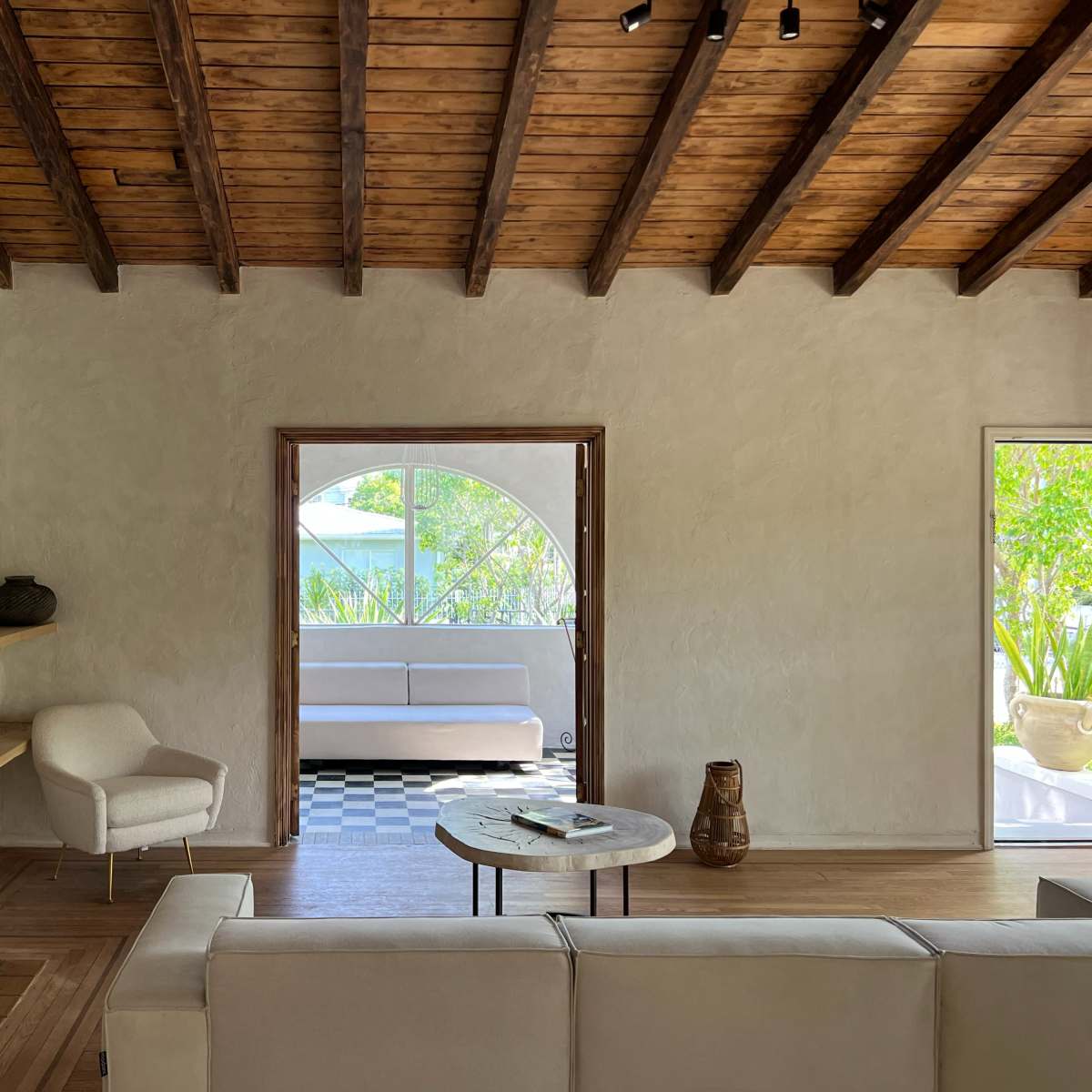 A spacious living room features a white sofa, a wooden coffee table, and a large arched window that opens to a green outdoor space.
