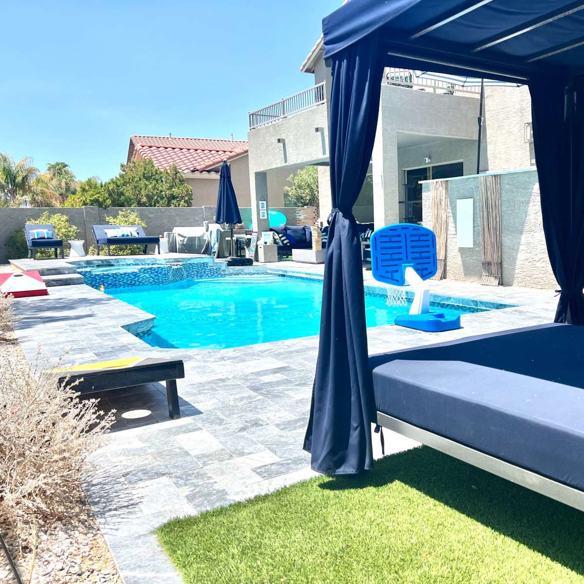 A modern outdoor pool area with a blue pool, lounge chairs, and a shaded seating area.