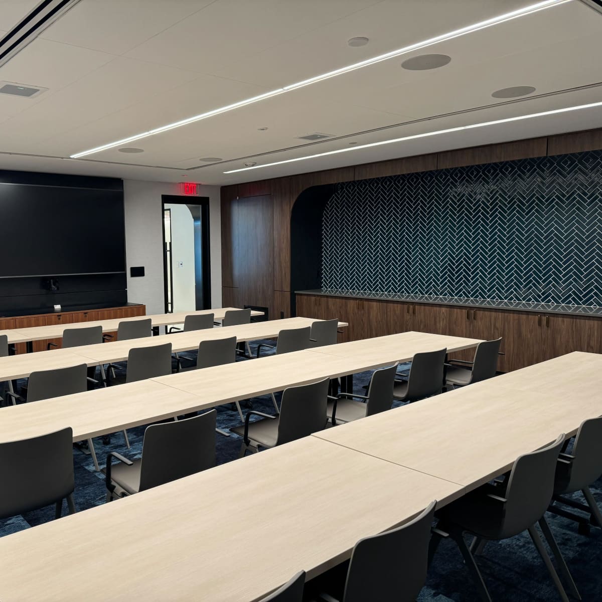 A modern conference room set up with multiple long tables and chairs, a large screen on the wall, and a podium in the corner.