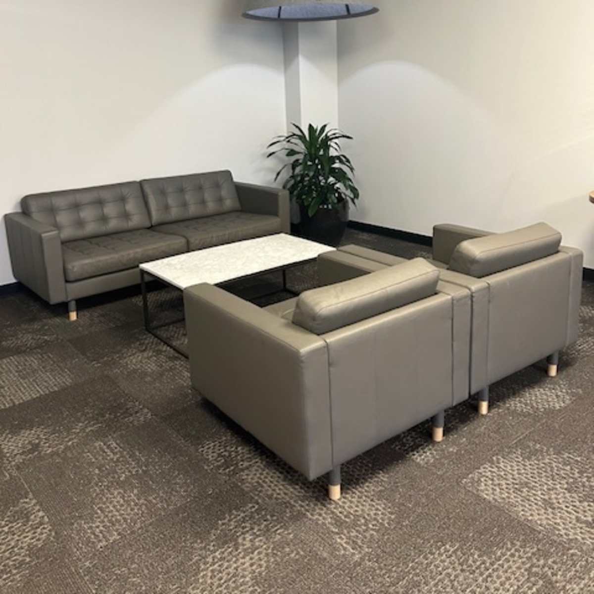 A minimalistic seating area with two gray sofas, a coffee table in the center, and a large pendant light above, surrounded by a potted plant.