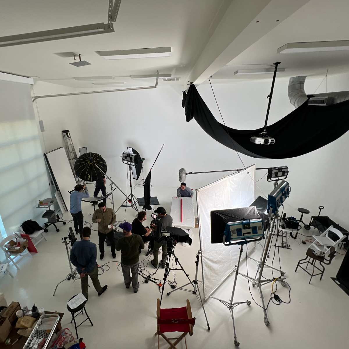 A film crew sets up equipment in a bright studio for a production shoot.