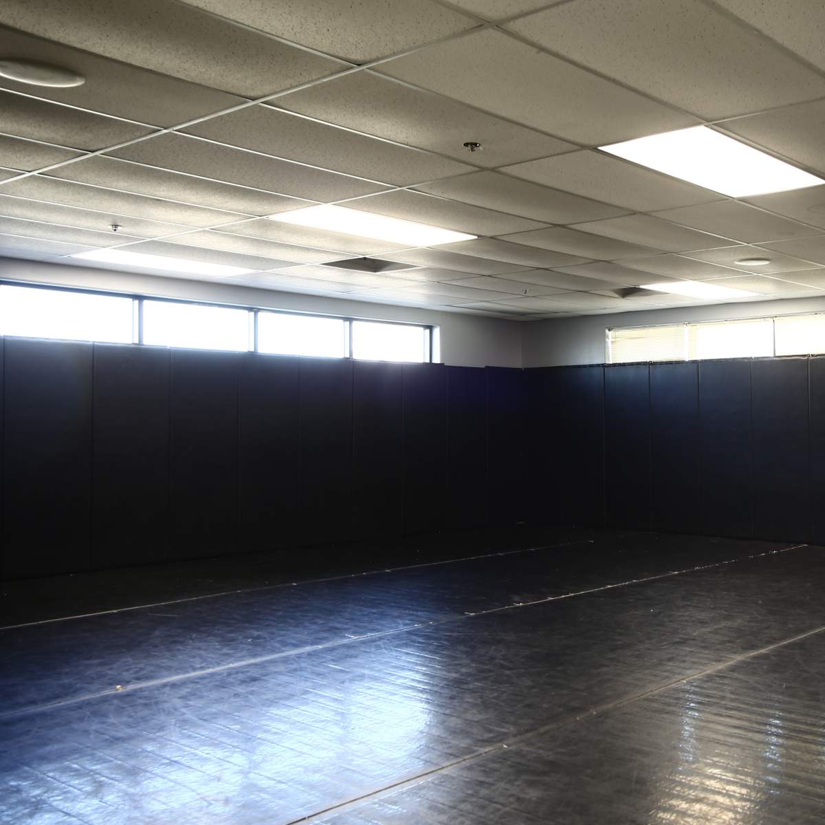 An unobstructed indoor space with black mats and padded walls, illuminated by overhead lighting.
