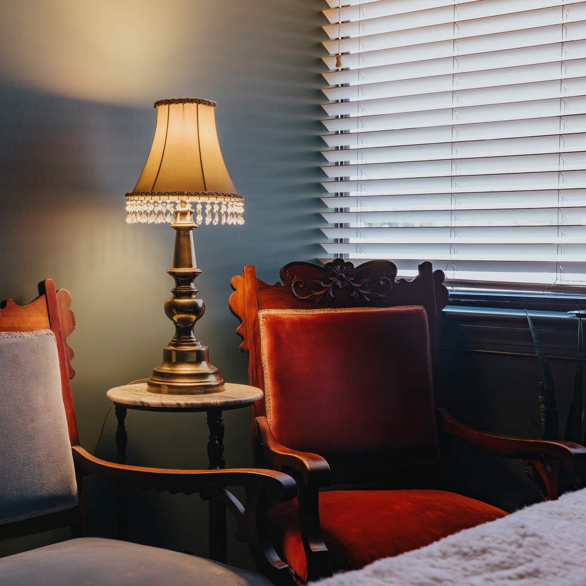 A vintage sitting area features two upholstered chairs and a brass lamp with a fringed shade on a side table.