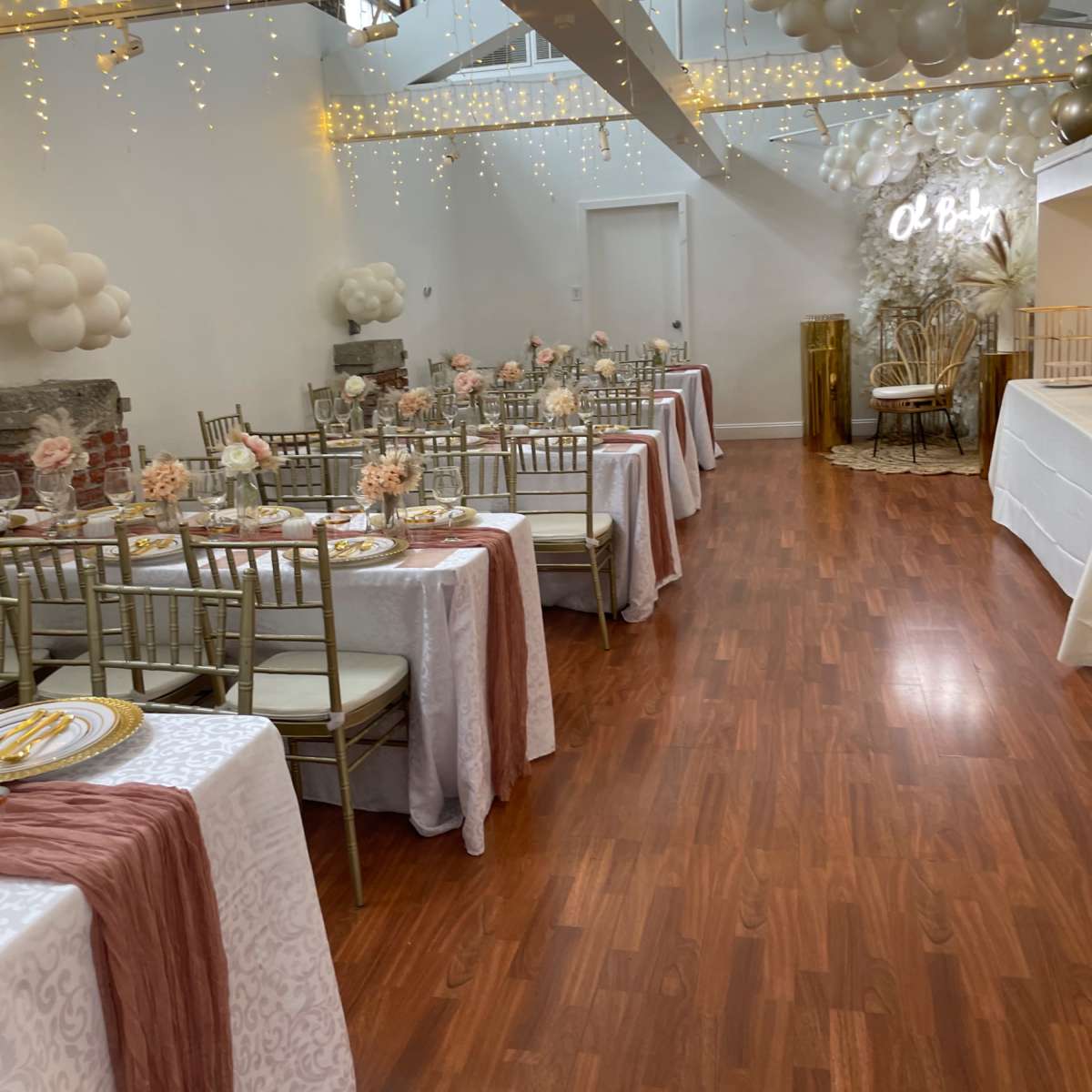 A decorated event space with tables set for a gathering, featuring floral centerpieces and string lights hanging from the ceiling.