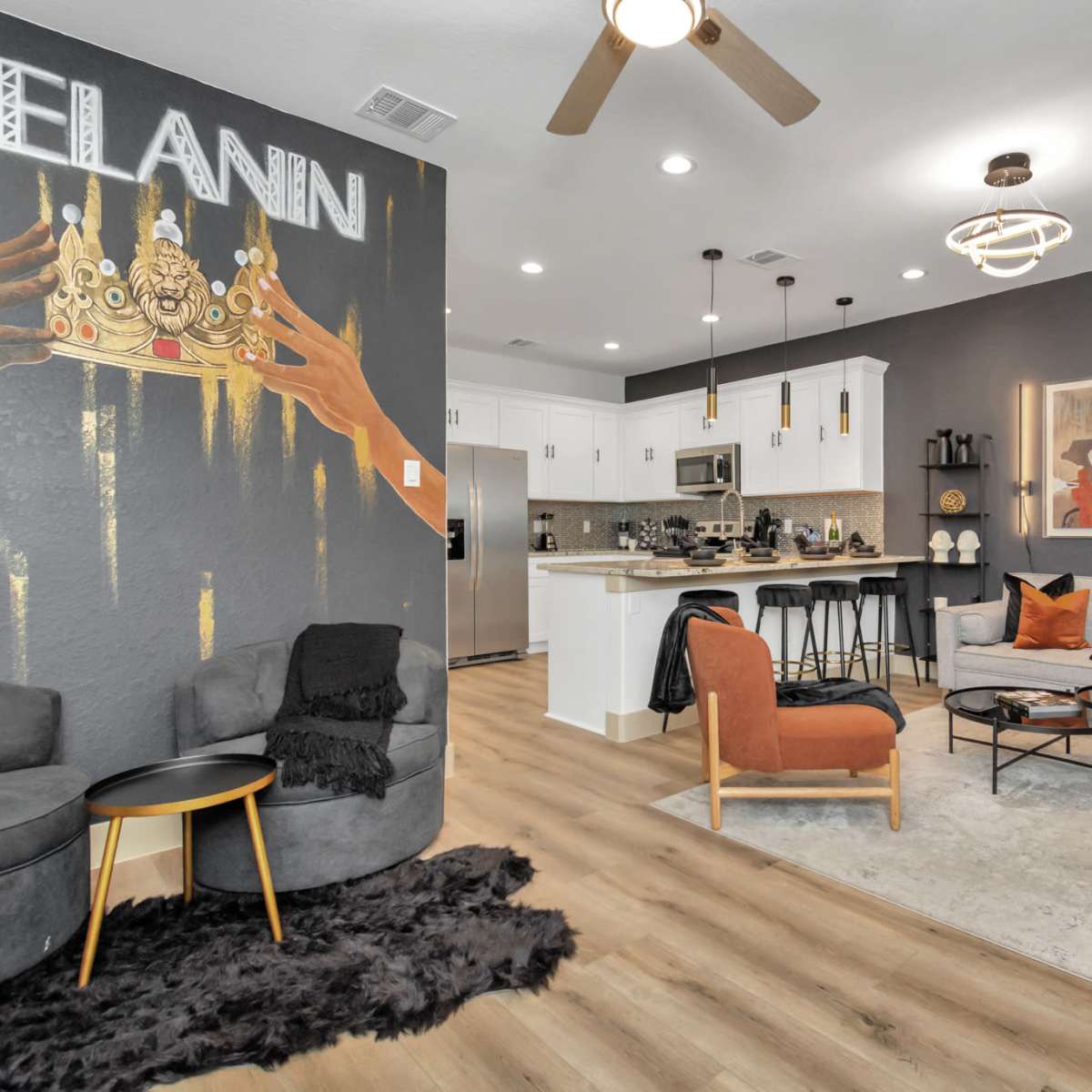 A stylish living area with modern furniture, a kitchen visible in the background, and a wall featuring artwork that highlights the word "MELANIN."