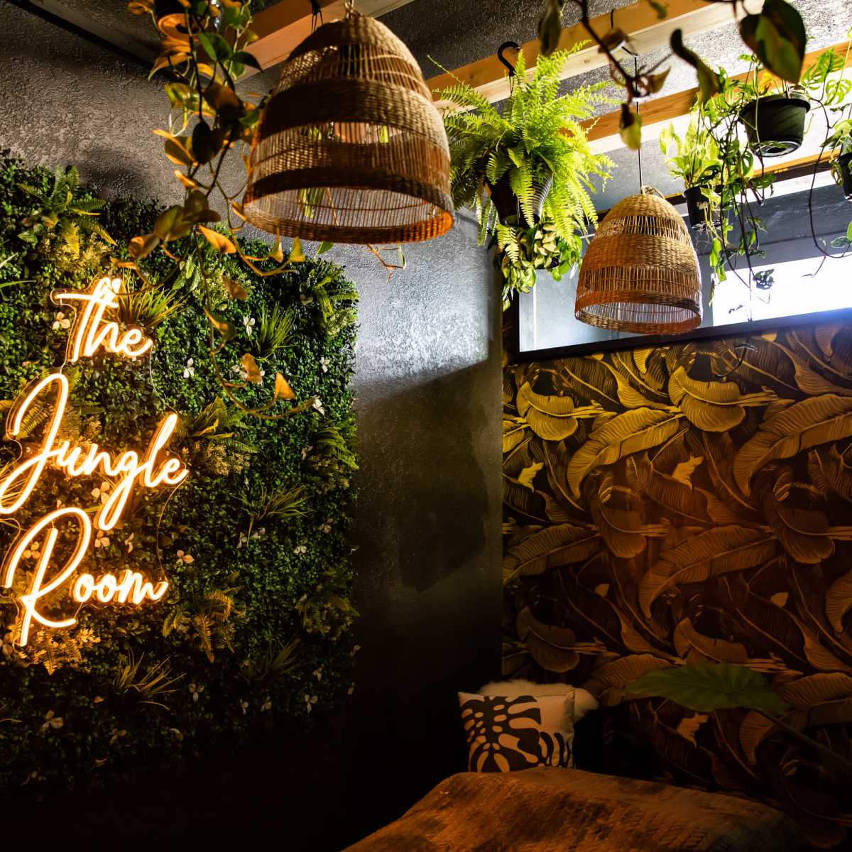 A room decorated with a neon sign that reads "The Jungle Room," surrounded by greenery and hanging light fixtures.