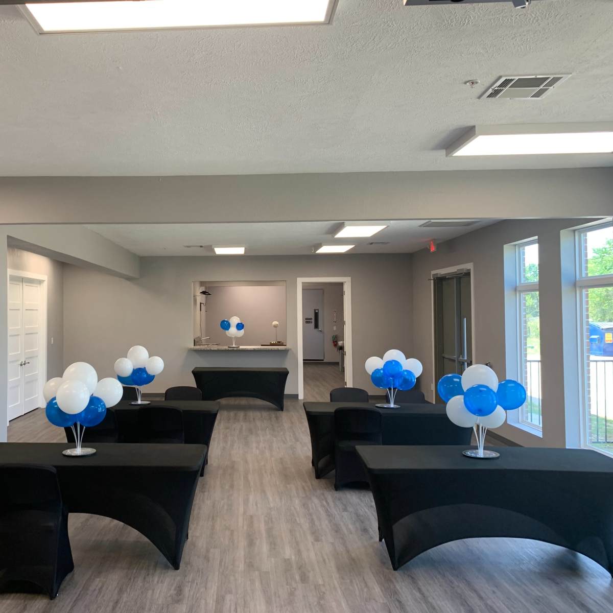 A large, well-lit room arranged with several black tables, each decorated with blue and white balloon centerpieces.