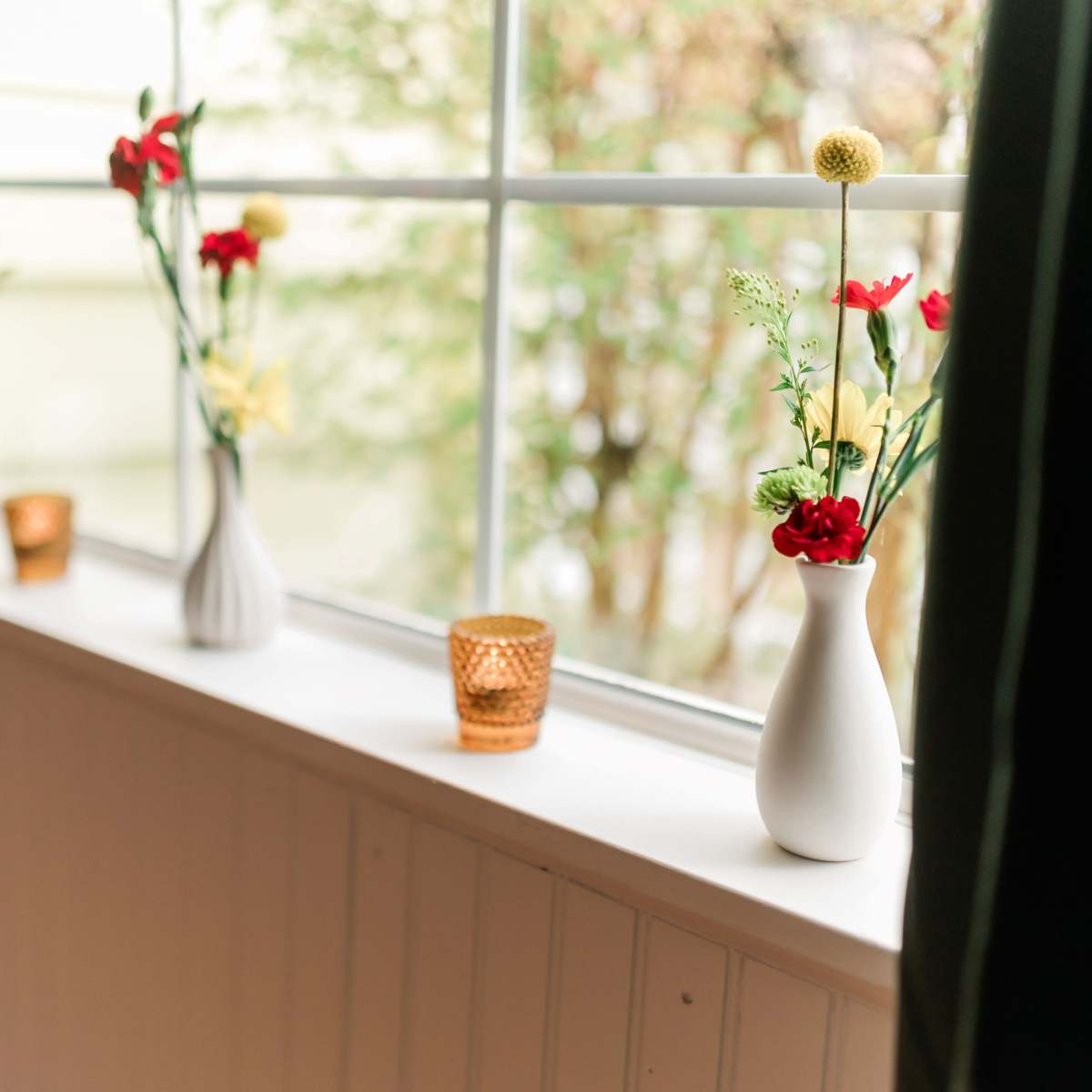 A window sill decorated with vases containing flowers and small candle holders.